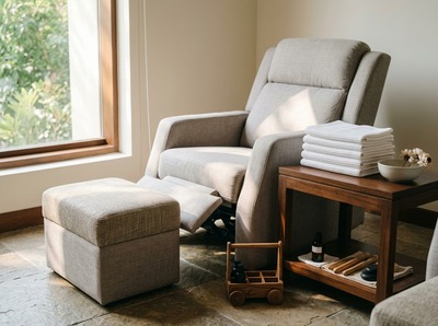 A quiet treatment room with an empty reclined chair, a footstool and folded towels, lit by soft window light